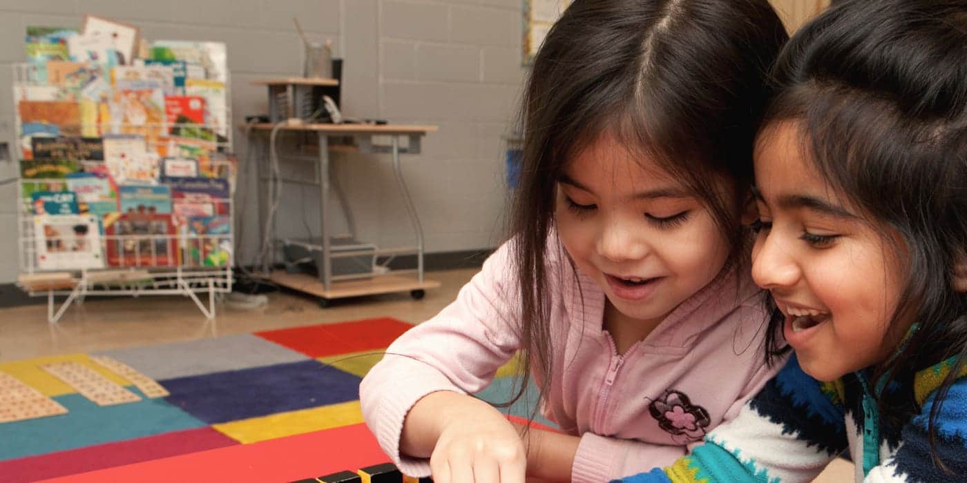 Two preschoolers laughing together while working with Montessori knobless cylinders